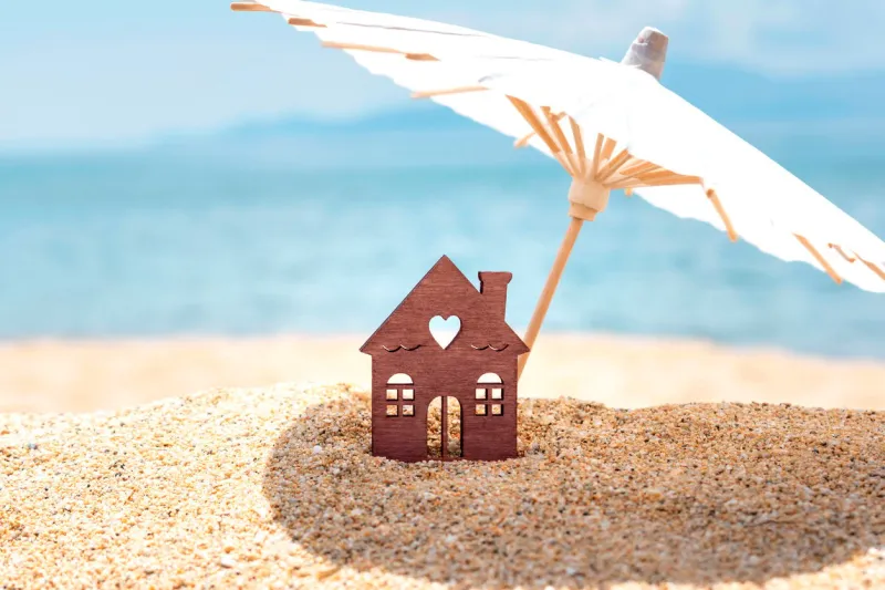 miniature house and umbrella on beach, blue sea and sky on blurred background real estate, sale or property investment concept symbol of dream home for family copy space