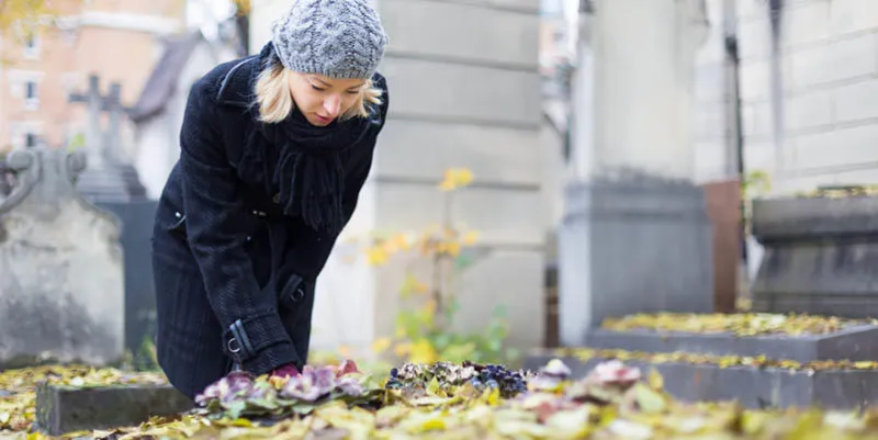 solitary woman mourning by gravestone, remembering dead relatives in on pere lachaise cemetery in paris, france