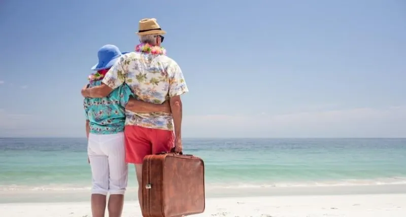 rear view of senior couple wearing a garland and holding suitcase on the beach