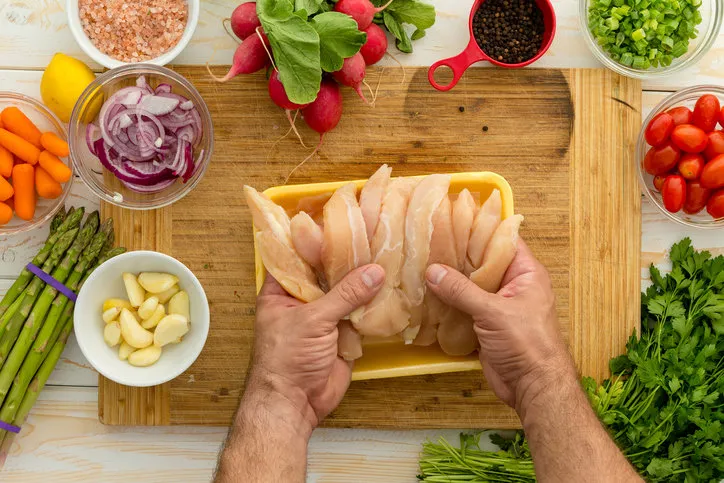 chef preparing chicken strips with vegetables and seasonings on cutting board for dinner perhaps lunch