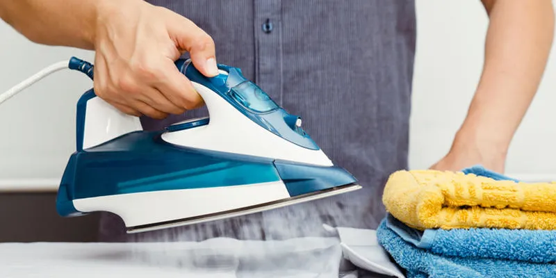 homme repasse les vêtements sur planche à repasser avec fer à vapeur bleu
