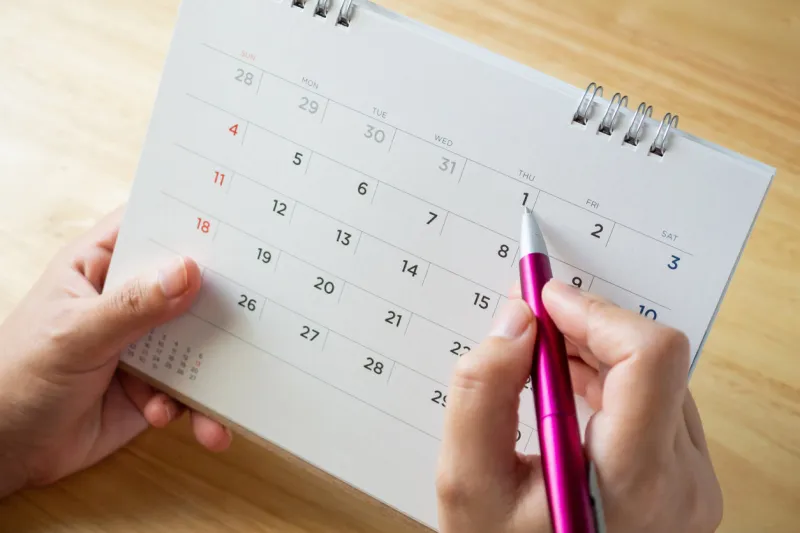 calendar page with female hand holding pen on desk table