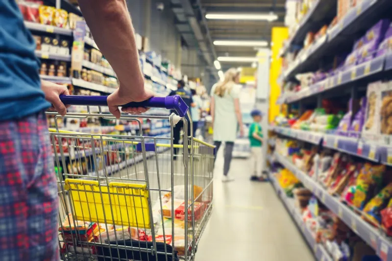 man with a basket walks in a supermarket hand and part of the basket in focus, blurred background