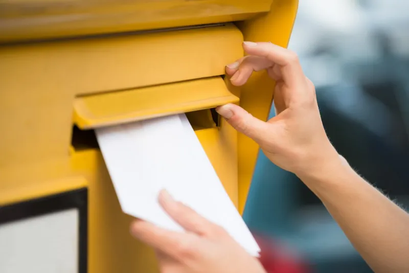 closeup of woman's hands inserting letter in mailbox