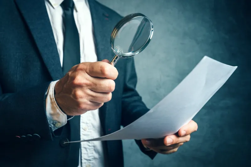 tax inspector investigating financial documents through magnifying glass, forensic accounting or financial forensics, inspecting offshore company financial papers, documents and reports