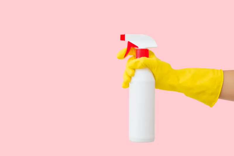 woman hand in yellow rubber protective glove holding white plastic spray bottle on pastel pink background general or regular cleanup empty place for text or logo side view closeup