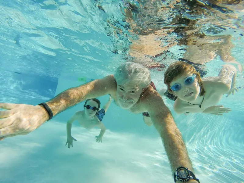 father, grandfather, and children swim underwater in pool in summer