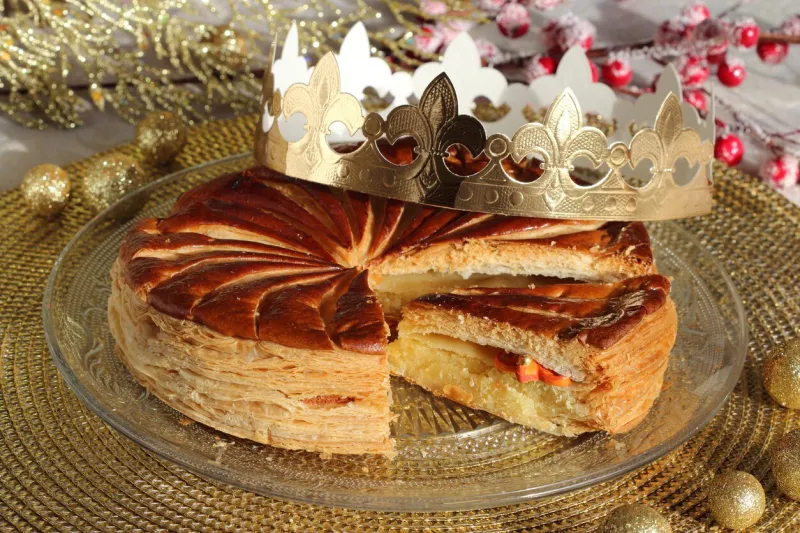 epiphany cake with a golden paper crown and one small porcelain charm inside on a glass plate on the holiday table slice of kings cake galette des rois