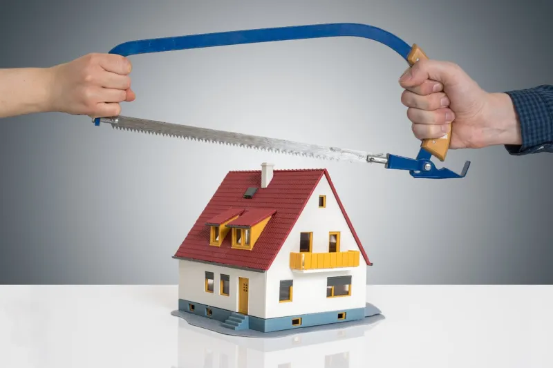 divorce and dividing a house concept man and woman are splitting model of house with saw
