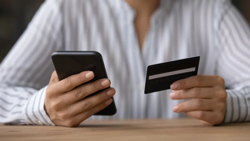 close up woman paying online by credit card, using smartphone, sitting at wooden desk, young female holding phone, browsing banking service, checking balance, shopping, making internet payment