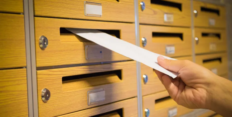 la main de mailman mettant l'enveloppe jaune dans la boîte aux lettres grise