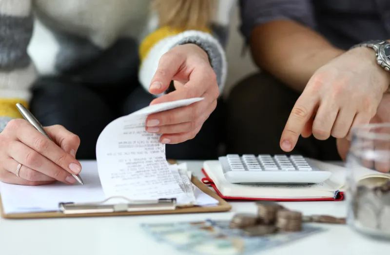 close-up view of man and woman making account of family income writing down and calculating expenses attentive review of finance calculator on desk economy concept