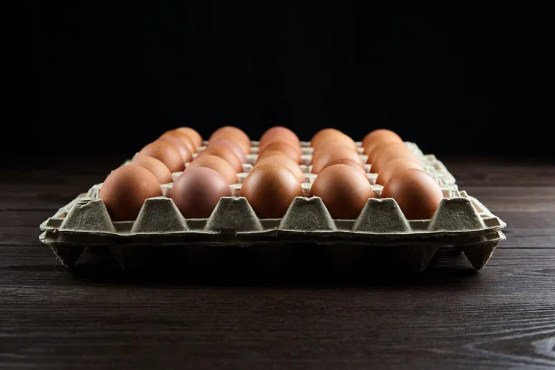 brown chicken eggs in recycled cardboard package on table, closeup, selective focus egg tray on wooden background