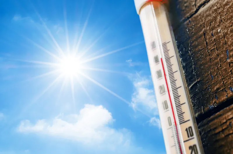 thermometer with a high temperature reading on a scale, against a background of bright sun and a blue sky with clouds the concept of hot, dangerous weather, global warming