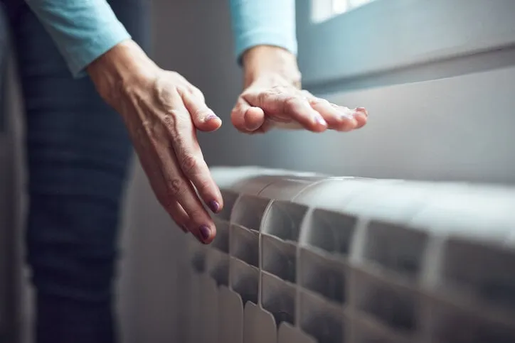 woman heating her hands on the radiator during cold winter days