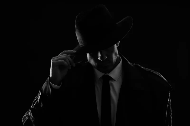 old fashioned detective in hat on dark background, black and white effect