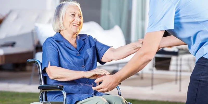 midsection of male caretaker helping senior woman to get up from wheelchair at nursing home lawn