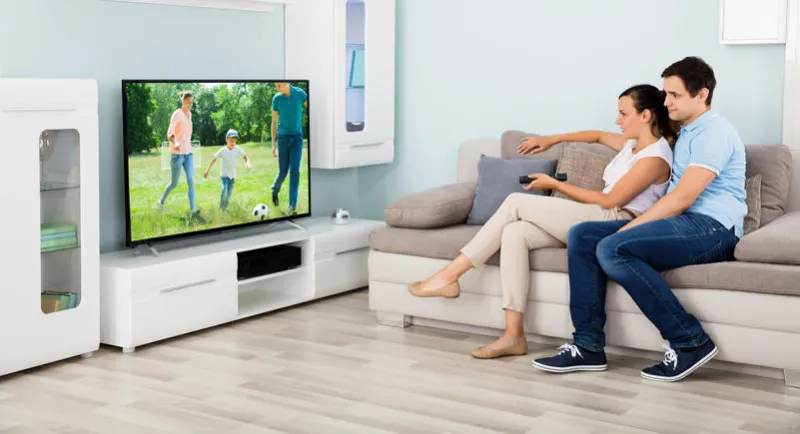 couple heureux, regarder la télévision ensemble tout en étant assis sur le canapé à la maison