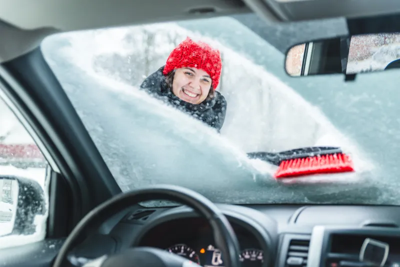 young pretty woman cleaning car after snow storm blizzard
