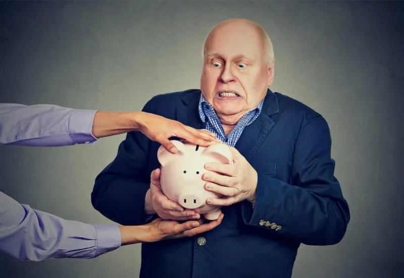 elderly upset scared business man holding piggy bank trying to protect his savings from being stolen isolated gray background