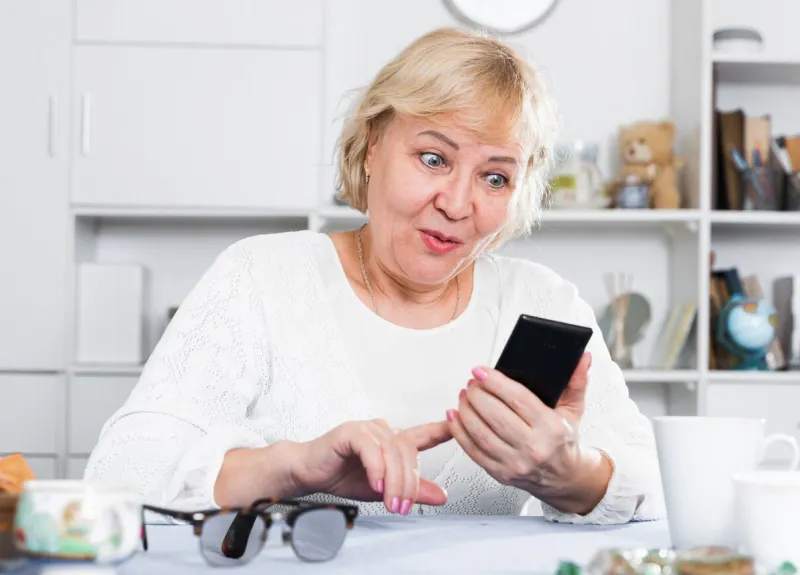 mature woman enjoys a modern smartphone while sitting at home at a table