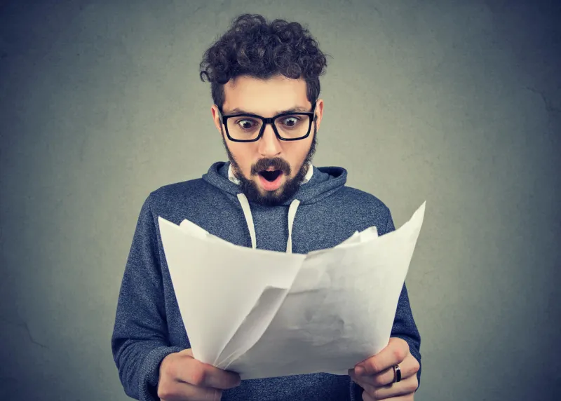 handsome man in eyeglasses exploring documents and looking shocked with results
