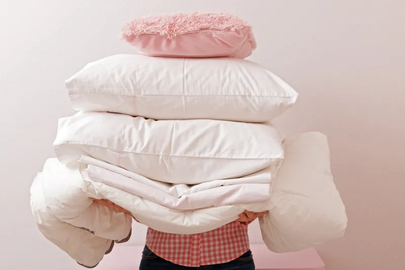 woman holding a pile of bedding for sleeping household