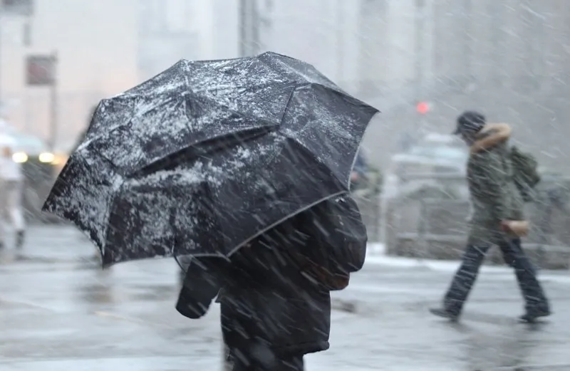 this is a photograph of a pedestrian in a snow storm with an aumbrella with a person in the background without an umbrella