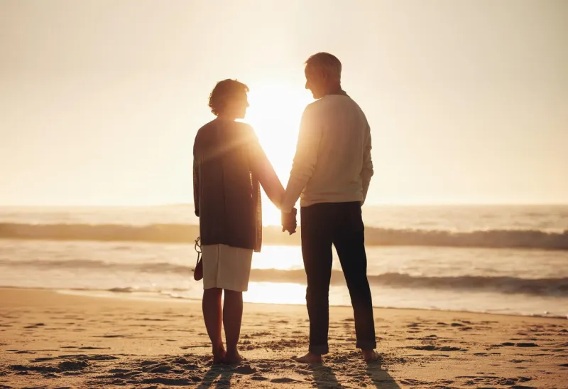 rear view of a senior couple holding hands on the beach mature couple standing together on a seashore at sunset