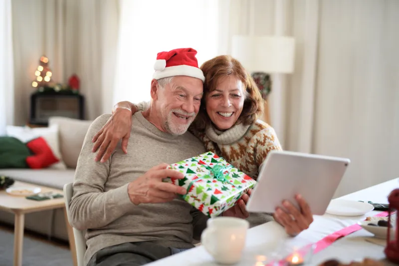 front view of happy senior couple indoors at home at christmas, having video call with family