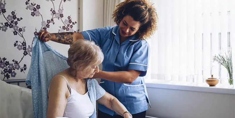 home caregiver helping a senior woman get dressed in her bedroom