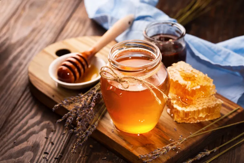 jar of liquid honey with honeycomb inside and bunch of dry lavender over old wooden table dark rustic style, selective focus