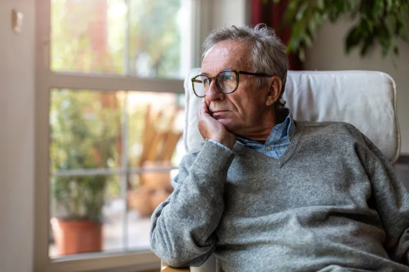 senior man looking out of window at home