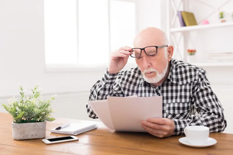 shocked senior man looking at bills in disbelief, holding his glasses on forehead, copy space