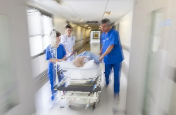 une photographie floue d'un patient sur un brancard ou une civière poussé à grande vitesse dans un couloir de l'hôpital par des médecins et des infirmières vers une salle d'urgence