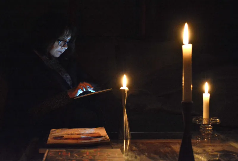 lifestylethis moody, dark, image shows a woman reading by candle light on her digital tablet, while awaiting the return of power to her home, after a widespread power outage