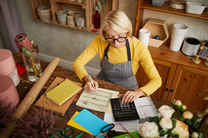 high angle portrait of female businesswoman counting finances using calculator in small shop, copy space