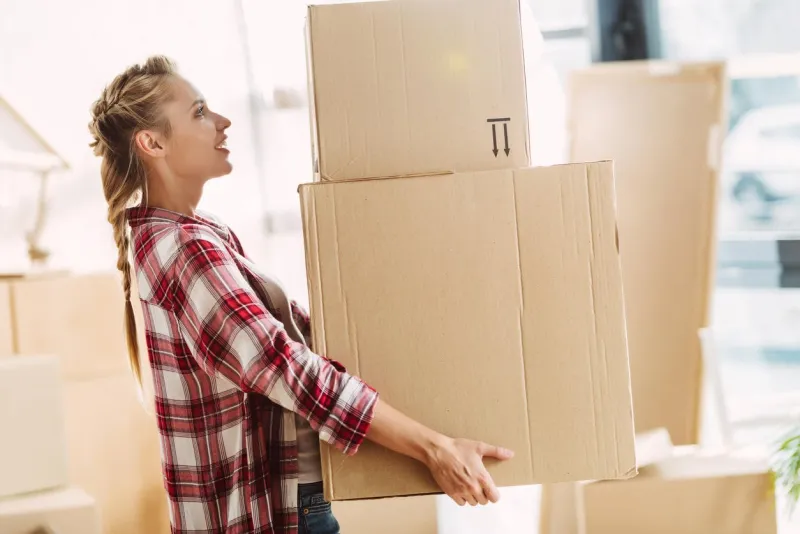 side view of pretty young woman holding cardboard boxes indoors