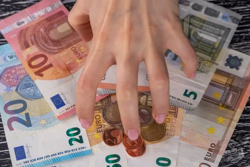 twisted by greed, the hand of the woman rakes up a bunch of euro notes and coins to yourself at a dark wooden table concept of division of property and family budget