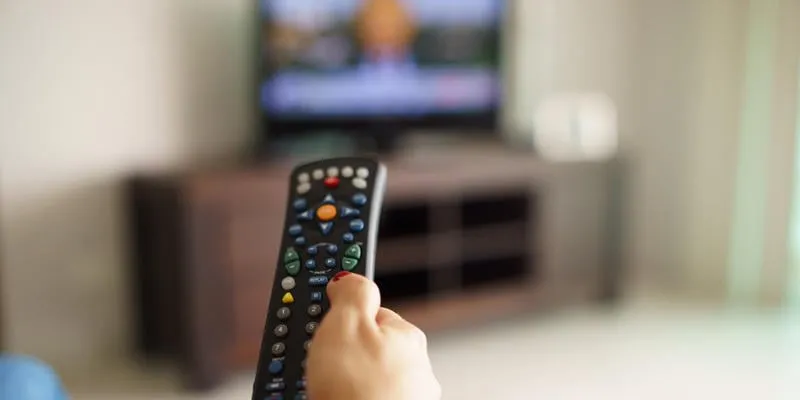 au-dessus de la vue de l'épaule de la jeune fille assise sur le canapé tenant la télévision à distance et des programmes de surf à la télévision