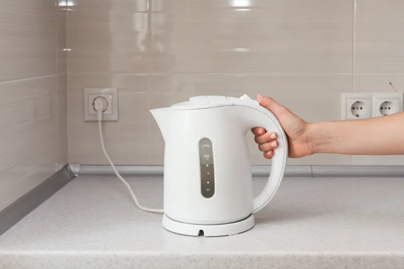 electric kettle in hand on the background of the kitchen