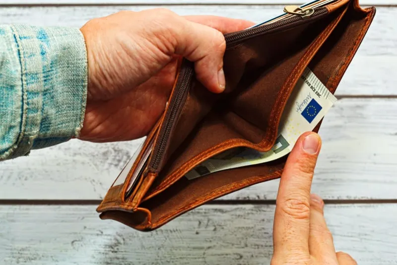 shabby leather wallet, almost empty, with just one 5 euro banknote, holding by male person in old and worn jeans jacket financial crisis idea