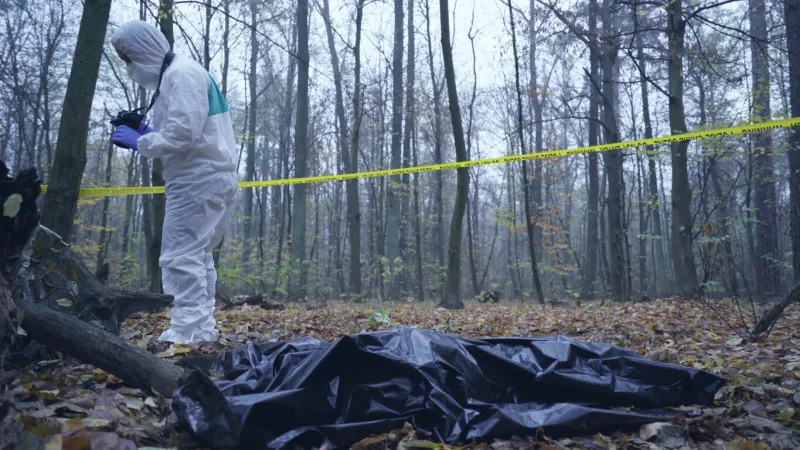 forensic expert photographs the crime scene, with the victim's body lying on the ground in a bag