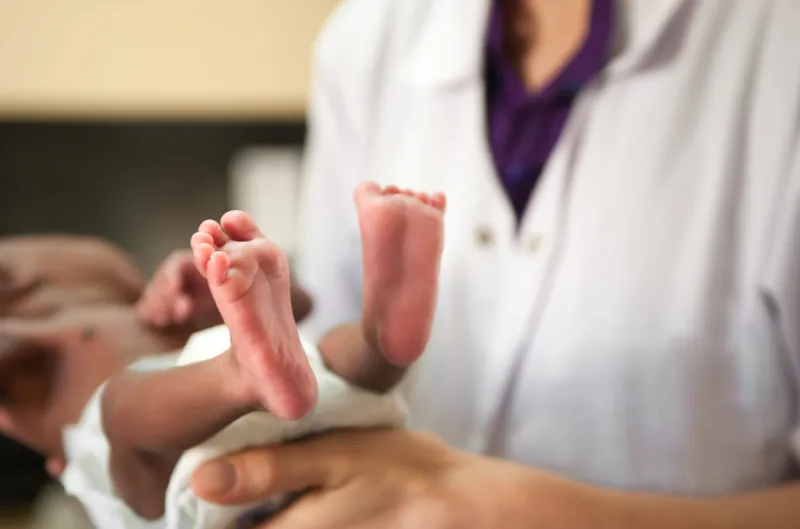 doctor or nurse is holding a baby baby's feet are most in focus baby is malnourished and tiny baby is wearing a diaper