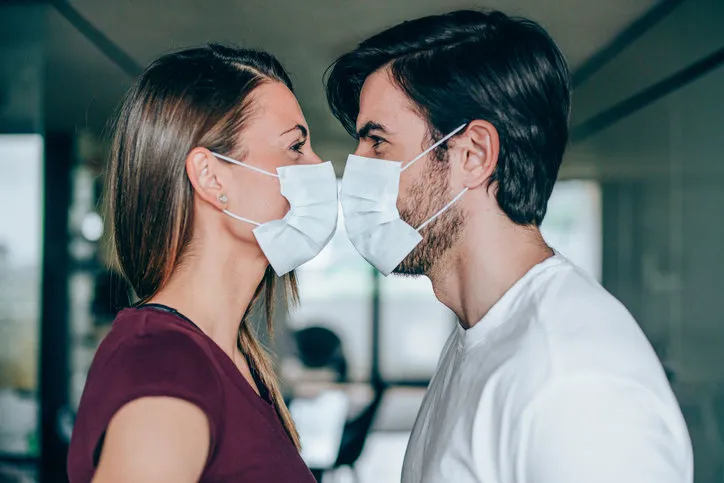 beautiful happy young couple wearing protective face masks and kissing each other side view of young man and young woman in medical masks kissing while they are in home isolation during coronavirus covid-19 quarantine