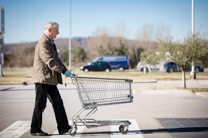 senior adult man pushing empty shopping cart on supermarket's parking lot