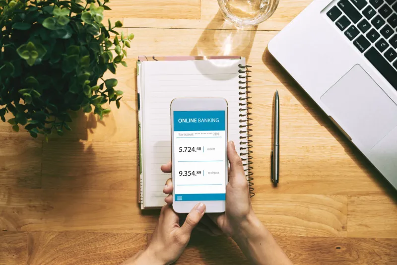 close-up shot of unrecognizable young woman using online banking application on smartphone while sitting at office desk, high angle view