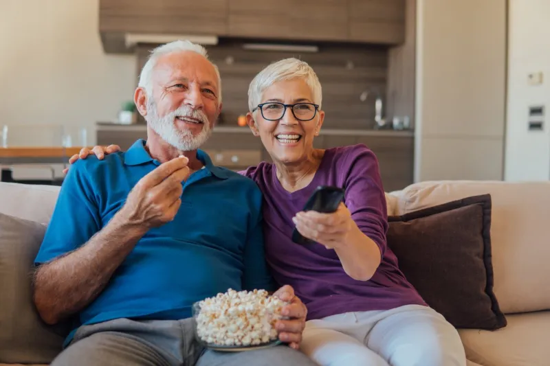 elderly couple eating popcorn and watching tv together