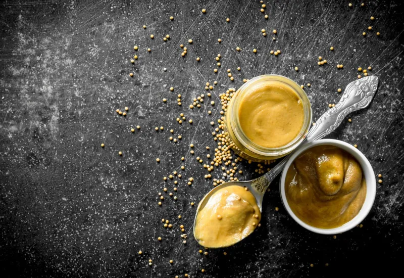 mustard in a glass jar, spoon and bowl on dark rustic background