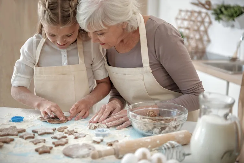 creative girl is making form of cookies from dough her face is all in flour old woman is looking at her creation with satisfaction and smiling